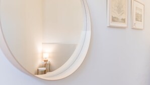 Un miroir rond est accroché à un mur blanc, et deux tableaux encadrés sont disposés au-dessus.
