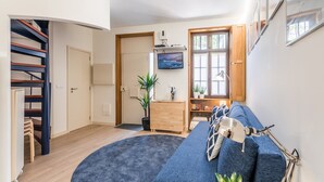 Un salon moderne avec un canapé bleu aux lignes courbes, un escalier en bois, un téléviseur à écran plat et une grande fenêtre offrant une vue dégagée.