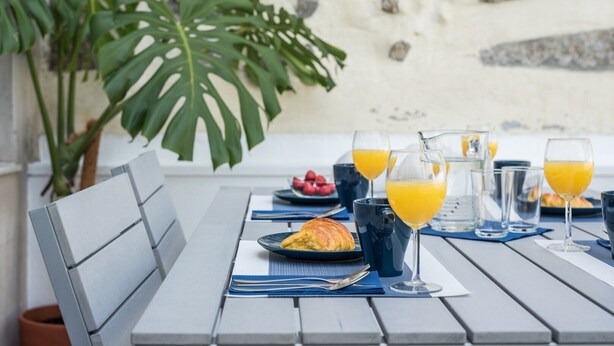 A table set for breakfast with a croissant, fruit, and glasses of orange juice. - GuestReady - Sunny patio paradise in Porto (Porto)