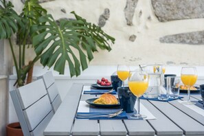 A table set for breakfast with a croissant, fruit, and glasses of orange juice. - GuestReady - Sunny patio paradise in Porto (Porto)
