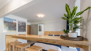 A modern, open-plan room with a wooden desk, bar stools, a large potted plant, and cityscape posters on the wall. - GuestReady - Sunny patio paradise in Porto (Porto)
