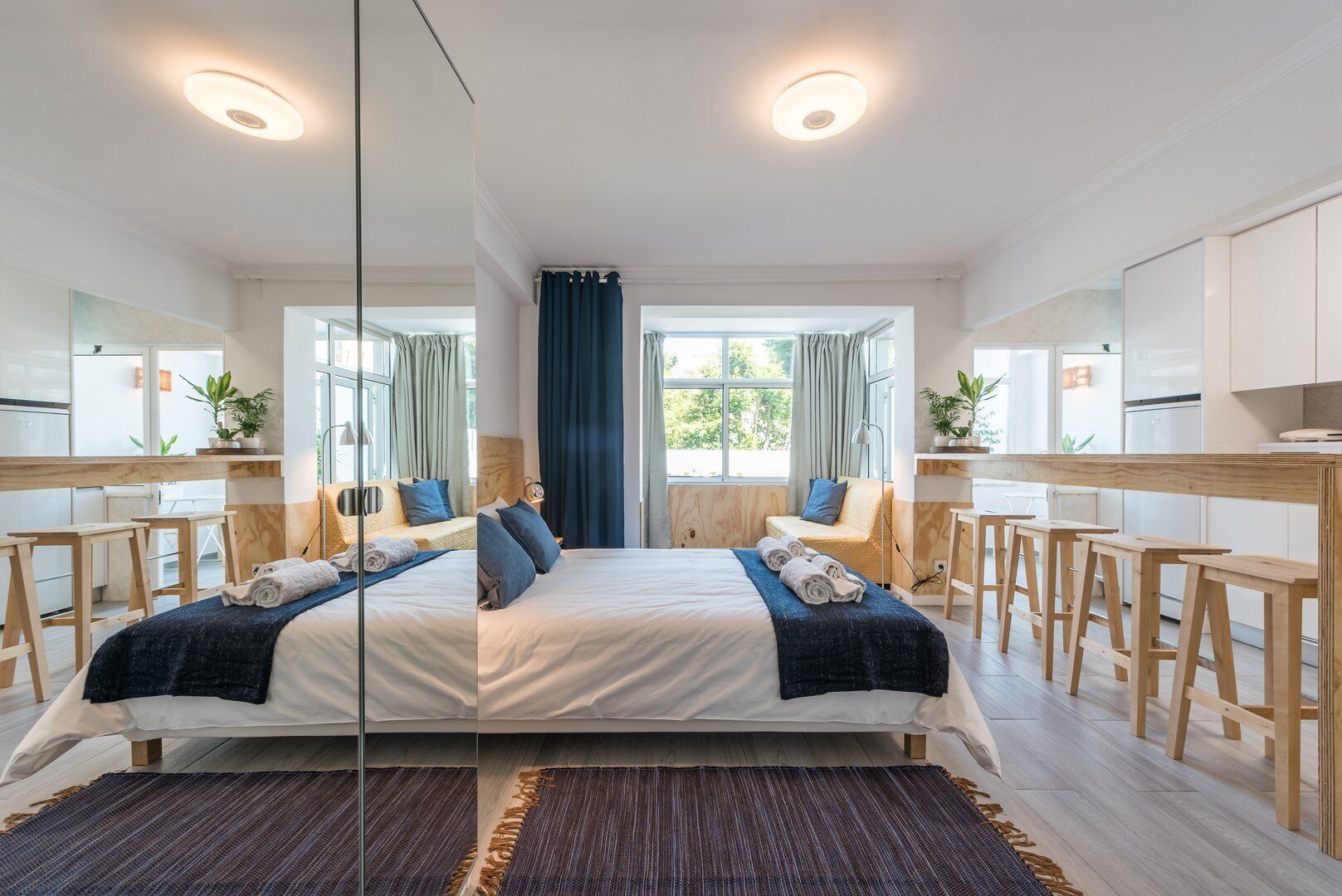 A modern hotel room with a large bed, a desk, and a kitchenette.