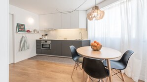 A modern kitchen with grey cabinets, a round dining table with black chairs, and a hanging light fixture. - GuestReady - Chic and cozy getaway (Porto)