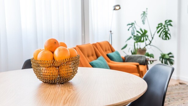 A dining table with a woven basket of oranges, an orange sofa, and a floor lamp in a bright room with large windows. - GuestReady - Chic and cozy getaway (Porto)