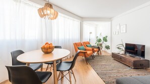 A modern living room with a round dining table, two orange armchairs, a sofa, a television, and a large window with sheer curtains. - GuestReady - Chic and cozy getaway (Porto)