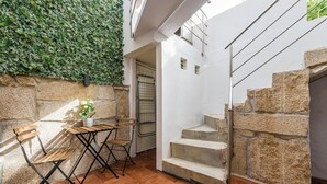 A patio with a stone wall, a wooden table with chairs, and a staircase.