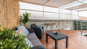 An outdoor patio with a sofa, two chairs, a small table, and a potted plant.