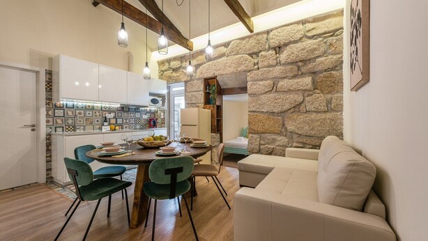A modern kitchen with a stone wall, a dining area with a round table and chairs, and a living room with a sofa.