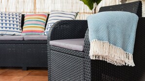 A wicker sofa with a cushion and a throw blanket.