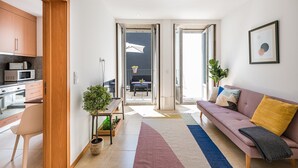 Eine moderne Wohnung mit Küche, einem Wohnbereich mit Sofa und Kissen sowie einem Balkon mit Sitzgelegenheit.