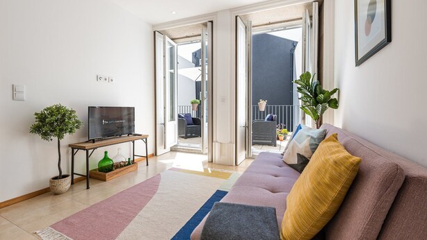 Ein modernes Wohnzimmer mit einer Couch, einem Fernseher, einem Couchtisch und einer Topfpflanze.