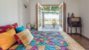 Een slaapkamer met een kleurrijk quilt, een houten nachtkastje en uitzicht op een balkon met een potplant.
