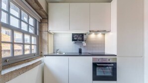 A modern kitchen with white cabinetry, a built-in oven, and a window with multiple panes. - GuestReady - Genuine Oporto Apts (Porto)