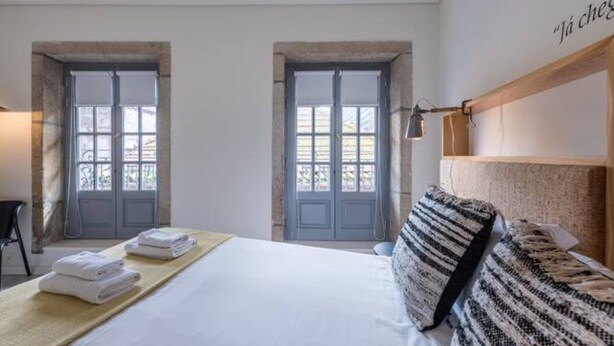 A hotel room with a bed, two windows, and a headboard with a lamp. - GuestReady - Genuine Oporto Apts (Porto)