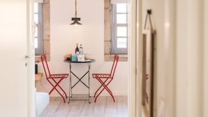 A small dining area with a table and two red chairs, a hanging light fixture, and a window with a view. - GuestReady - Genuine Oporto Apts (Porto)