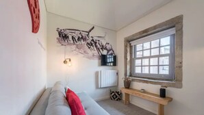 A modern living room with a grey sofa, a red pillow, a mounted TV, a wooden bench, and a window with a stone frame. - GuestReady - Genuine Oporto Apts (Porto)