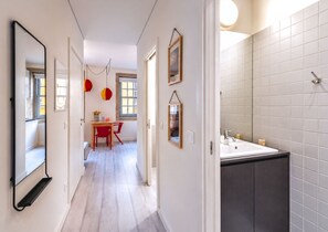 Ein Flur mit Essbereich, einem Spiegel und einem Badezimmer mit weißen Fliesen.