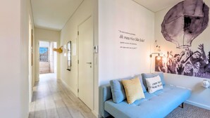 Una sala de estar moderna con un sofá azul claro, un mural en la pared y un pasillo que conduce a otra habitación.