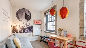Una habitación moderna con un sofá gris, sillas rojas, una mesa de madera, un ventanal y un televisor de pared.