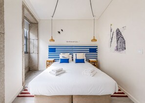 A bedroom with a striped headboard, a bed with white linens, two bedside tables, and a hanging light fixture. - GuestReady - Genuine Oporto Apts (Porto)