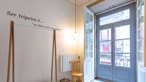 Una habitación con un banco, un taburete, un radiador, un cubo de basura y una puerta con ventanas.