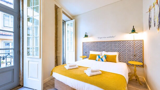 Habitación de hotel con cama, cabecero fijado a la pared, una mesita y una puerta que da a un balcón.