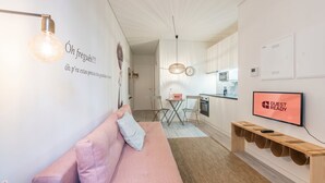 Een moderne woonkamer met een roze bank, een televisie en een keuken op de achtergrond.