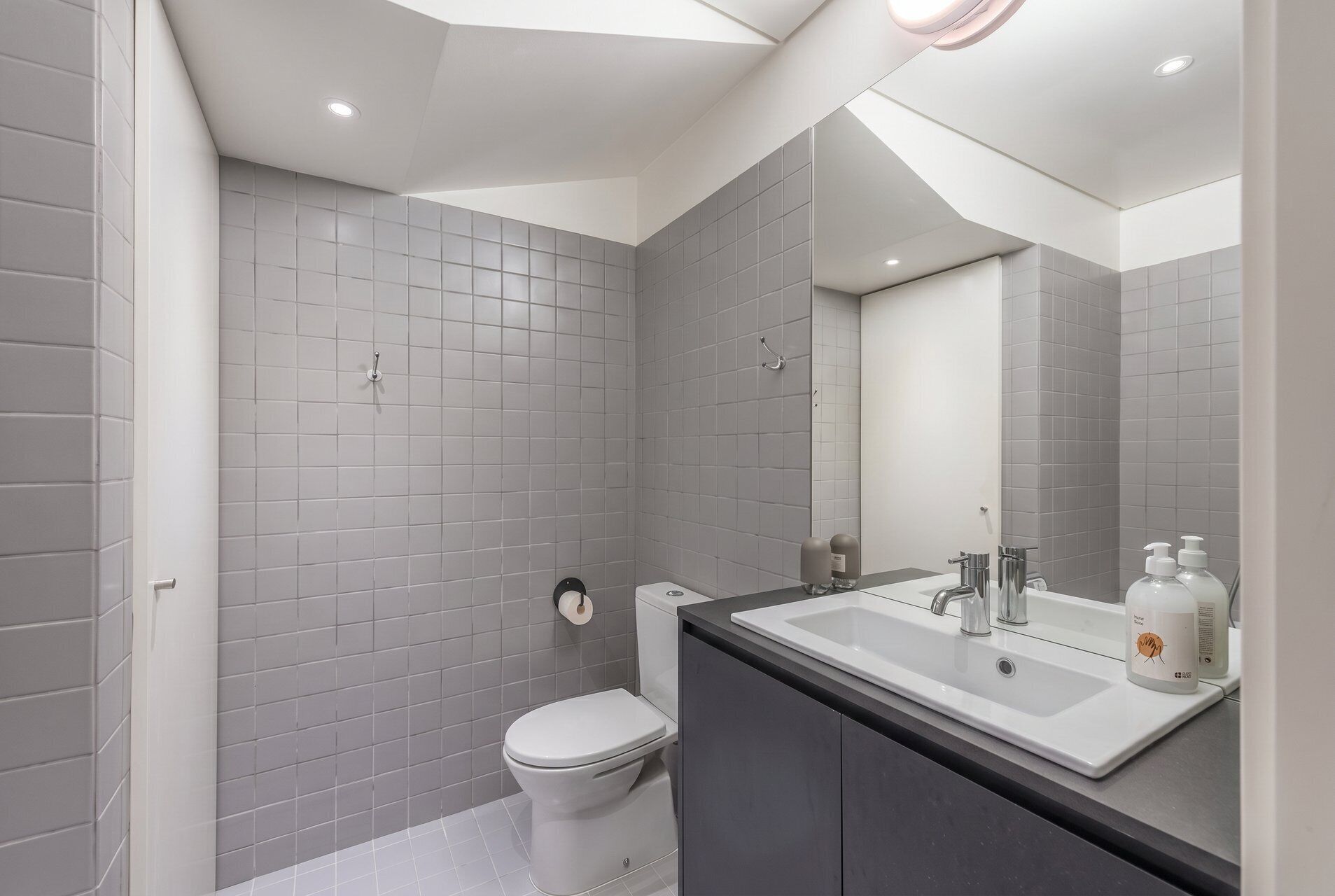 Ein modernes Badezimmer mit grauen Fliesen, einer weißen Toilette, einem Waschbecken mit Spiegel und einer Duschkabine.