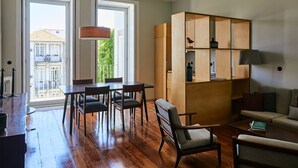 A spacious living room with a wooden coffee table, a sofa, and a dining area with chairs and a table. There is a bookshelf with various items on it. - GuestReady - Picaria Living Quarter 1 (Porto)