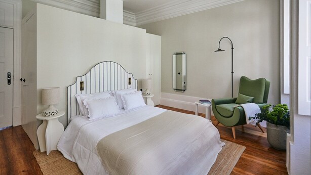A bedroom with a large bed, a green armchair, a mirror, and a small table with a lamp. - GuestReady - Picaria Living Quarter 1 (Porto)