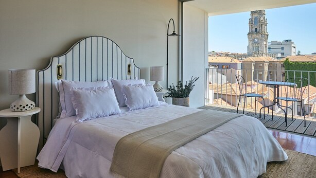Une chambre à coucher avec un lit, des tables de chevet, une lampe et une vue sur un paysage urbain avec des immeubles et une tour.