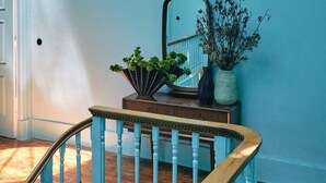 Un escalier avec des rampes peintes en bleu et une main courante en bois, menant à un palier agrémenté d’un miroir et d’un vase de fleurs séchées.