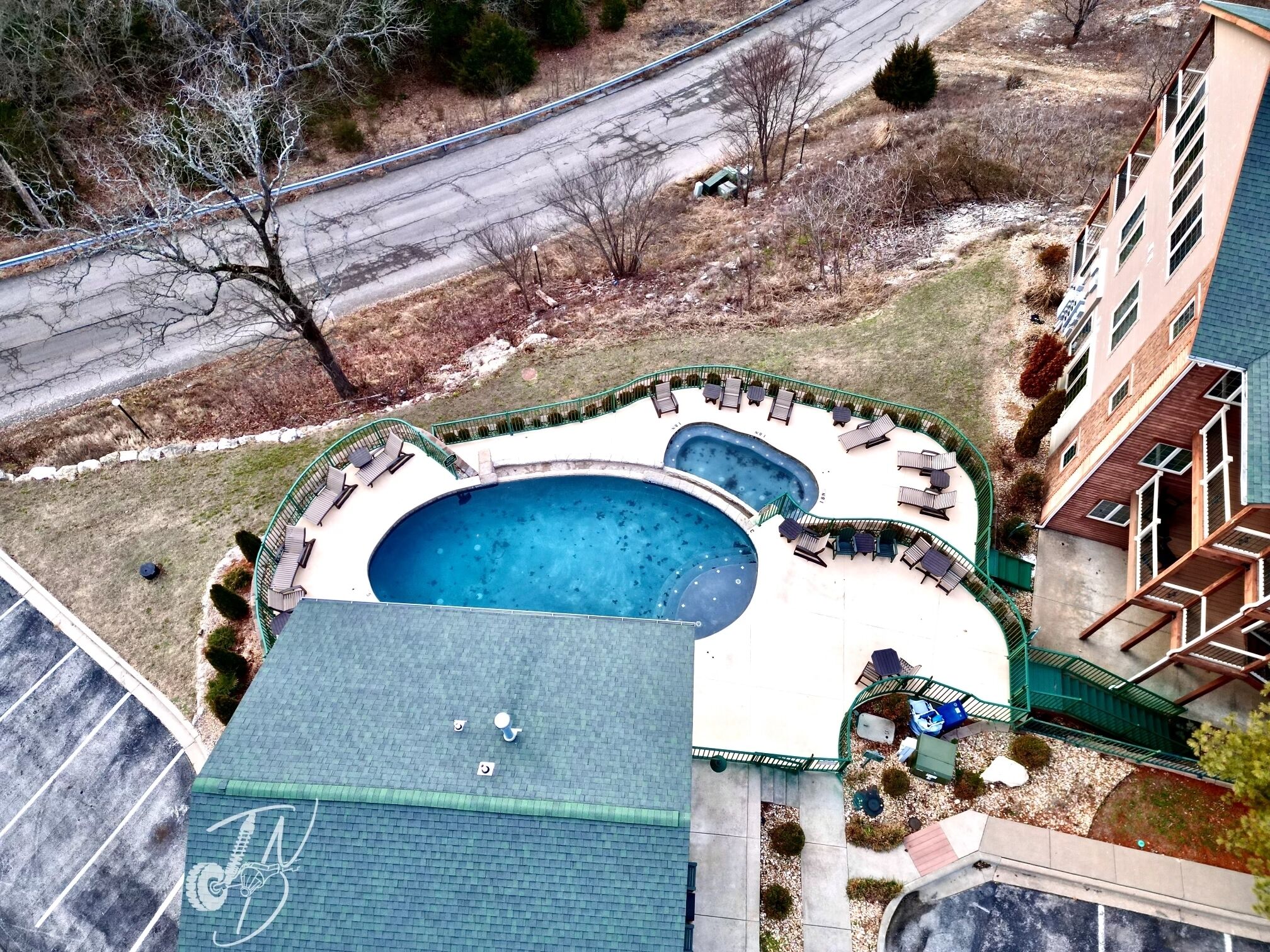 A rooftop swimming pool with lounge chairs and a small hot tub, surrounded by a green fence.