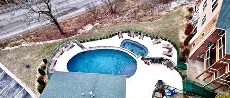 A rooftop swimming pool with lounge chairs and a small hot tub, surrounded by a green fence.