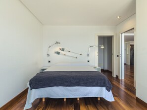 A modern bedroom with a large bed, two bedside lamps, and a wooden floor.