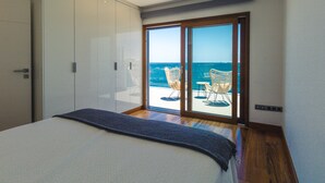 A bedroom with a large bed, a wardrobe, and a sliding glass door leading to a balcony with two wicker chairs and a view of the sea. - Taliarte Lighthouse Top Views Marea (Taliarte)