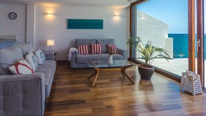 A modern living room with a sofa, a coffee table, and a potted plant. There is a large window offering a view of the ocean. - Taliarte Lighthouse Top Views Marea (Taliarte)