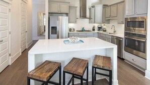 Una cocina moderna con armarios blancos, electrodomésticos de acero inoxidable y una isla central con taburetes.