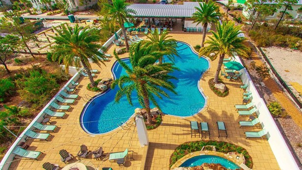Un área de piscina con sillones de descanso y palmeras.