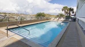 A rectangular swimming pool with a metal ladder, surrounded by a white fence. There are lounge chairs and umbrellas on the right side. - Fort Walton Beach Condo | Complimentary Seasonal Beach Service & More! (Fort Walton Beach)