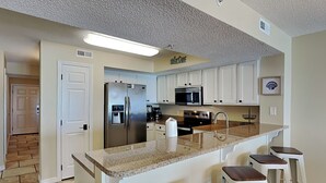 A kitchen with white cabinets, a stainless steel refrigerator, a microwave, and a granite countertop. - Fort Walton Beach Condo | Complimentary Seasonal Beach Service & More! (Fort Walton Beach)