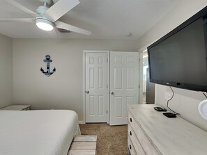 Un dormitorio con cama, cómoda, televisor, ventilador de techo y una puerta.