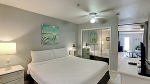 A bedroom with a bed, nightstand, lamp, ceiling fan, and a painting on the wall. - Island Mist B | The Beach is Your Backyard, Just Steps from the Sand! (Fort Walton Beach)