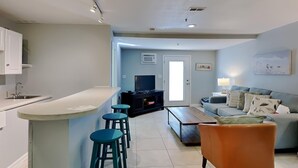 A modern kitchen with a bar area, a living room with a sofa and a TV, and a dining area with a wooden table. - Island Mist B | The Beach is Your Backyard, Just Steps from the Sand! (Fort Walton Beach)