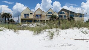 A beachfront property with multiple balconies and large windows, surrounded by sand and sparse vegetation. - Island Mist B | The Beach is Your Backyard, Just Steps from the Sand! (Fort Walton Beach)