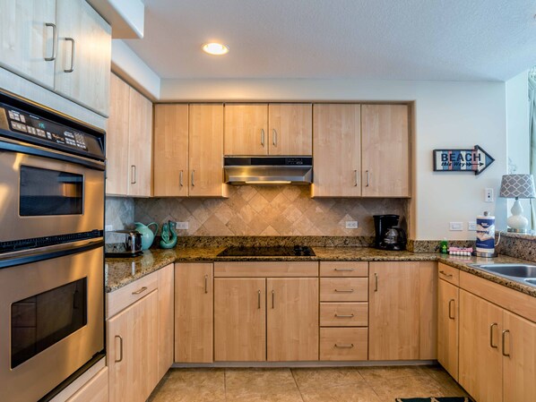 A modern kitchen with wooden cabinets, a stainless steel oven, a microwave, a coffee maker, and a tiled backsplash.