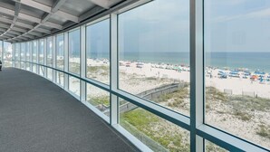 Een gang met grote ramen die uitzicht bieden op een strand met parasols en een zandpad.