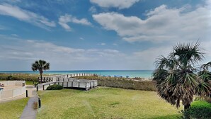 A beachside view with a wooden boardwalk leading to a beach area with umbrellas. - Regency Towers #203 West | Beach + Pool Access! (Pensacola Beach)