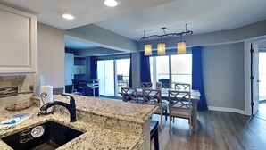 A modern kitchen with a granite countertop, a built-in sink, and a dining area with a table and chairs. - Regency Towers #203 West | Beach + Pool Access! (Pensacola Beach)
