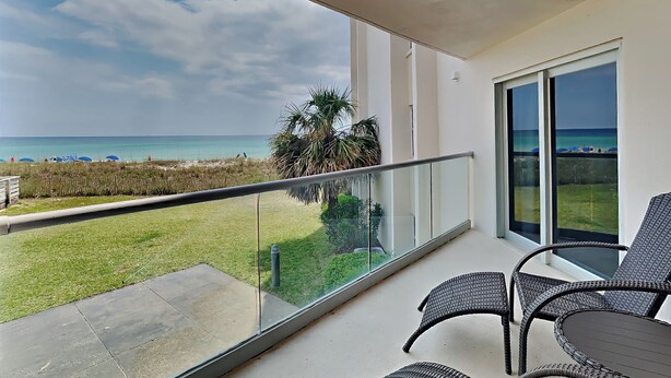 A balcony with a view of the beach, wicker furniture, and a glass railing. - Regency Towers #203 West | Beach + Pool Access! (Pensacola Beach)